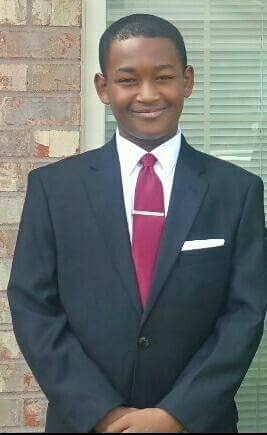 TJ dressed up in a navy suit with a red tie, smiling